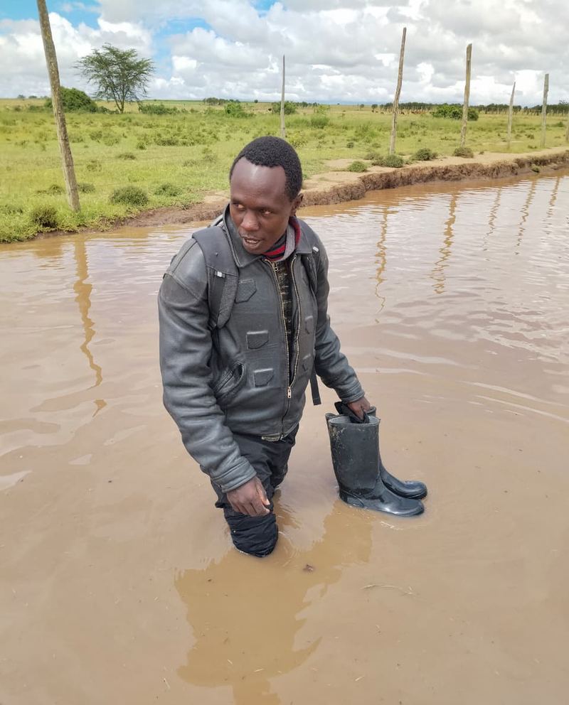 A Firstfield team member standing knee-deep in brown floodwater across the farm, boots in hand, after a flash flood