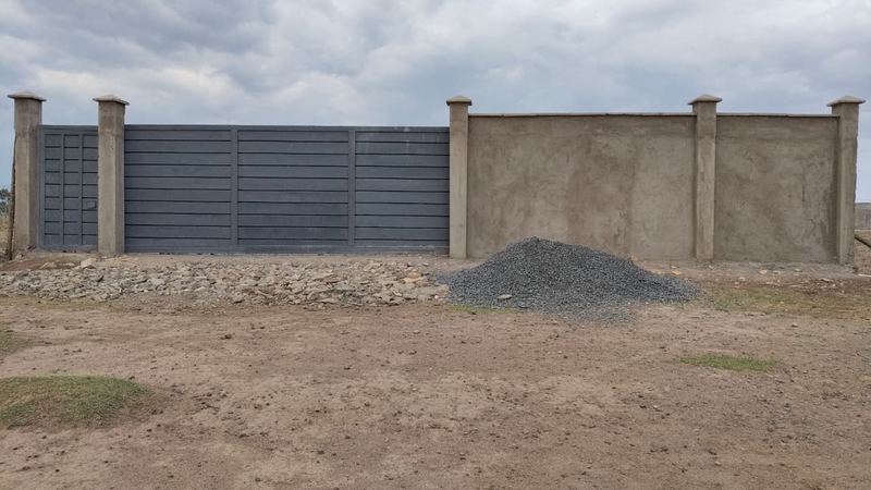 The Firstfield main gate at Olonini: a grey steel sliding gate between plastered pillars and a perimeter wall